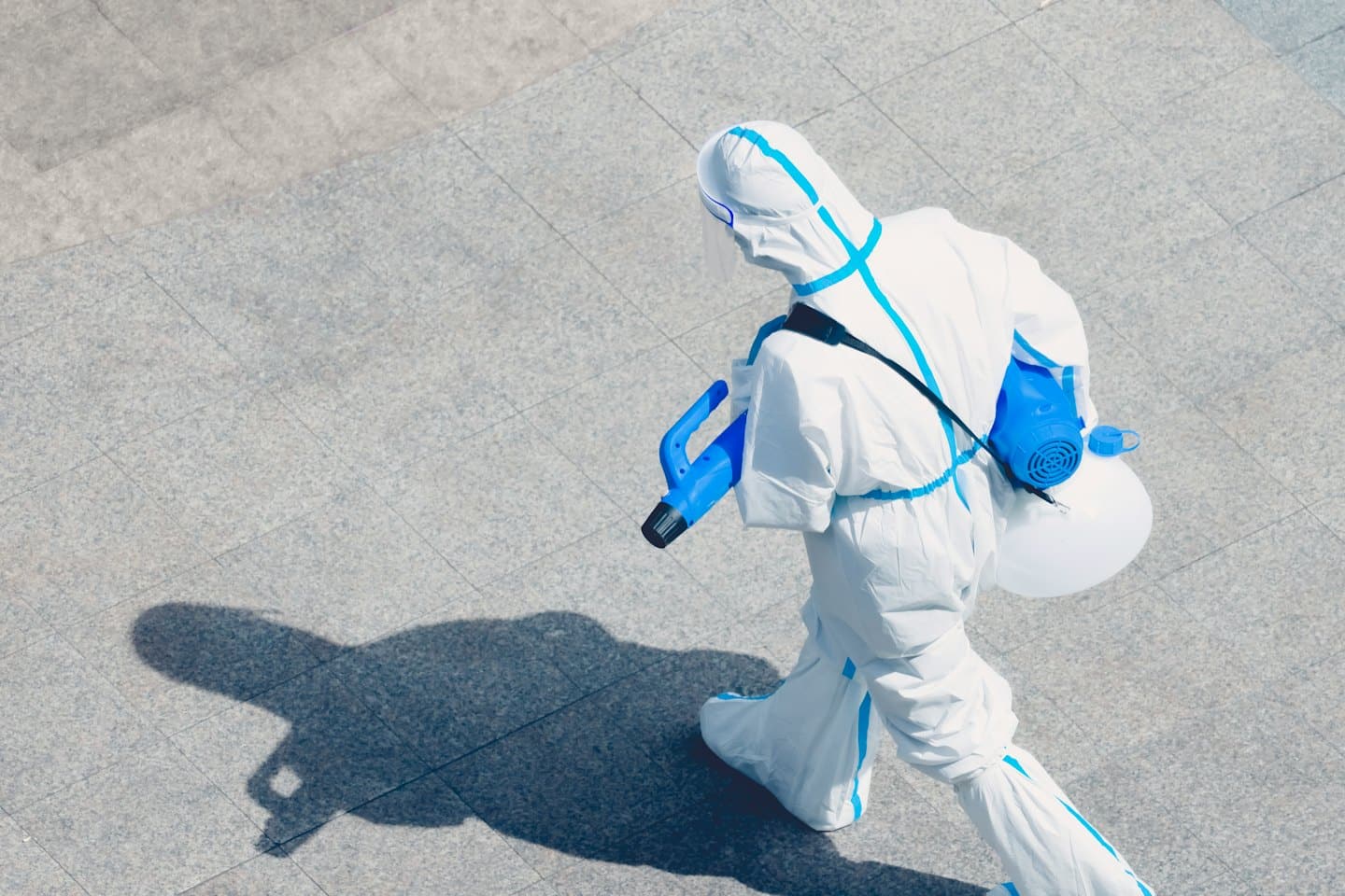 Hazmat tulumlu bir profesyonel dışarıda dezenfeksiyon püskürtücü taşıyor.