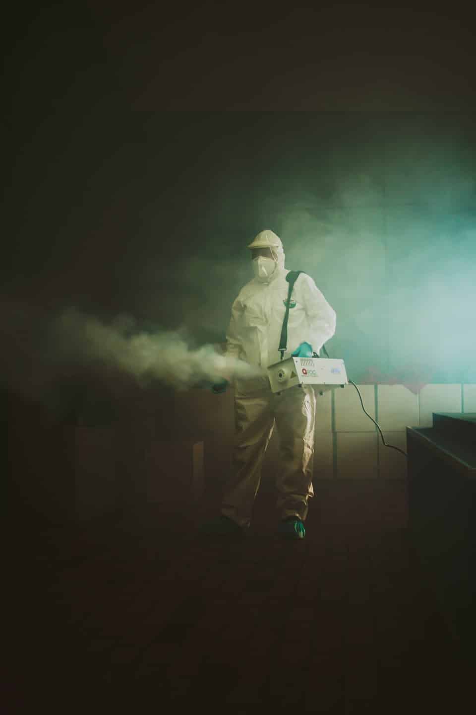 Hazmat tulumlu bir hijyen görevlisi sisleme makinesi kullanıyor.